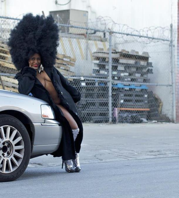 Akynos leaning against car in black coat and bling boots